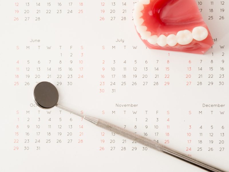 Dentist mirror tool and dentist demonstration teeth model with flesh pink gums on calendar; concept for dental appointment